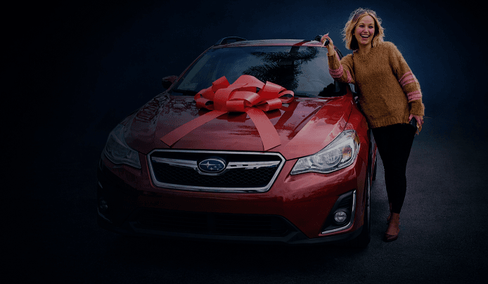 A happy woman leans against a new red Subaru.